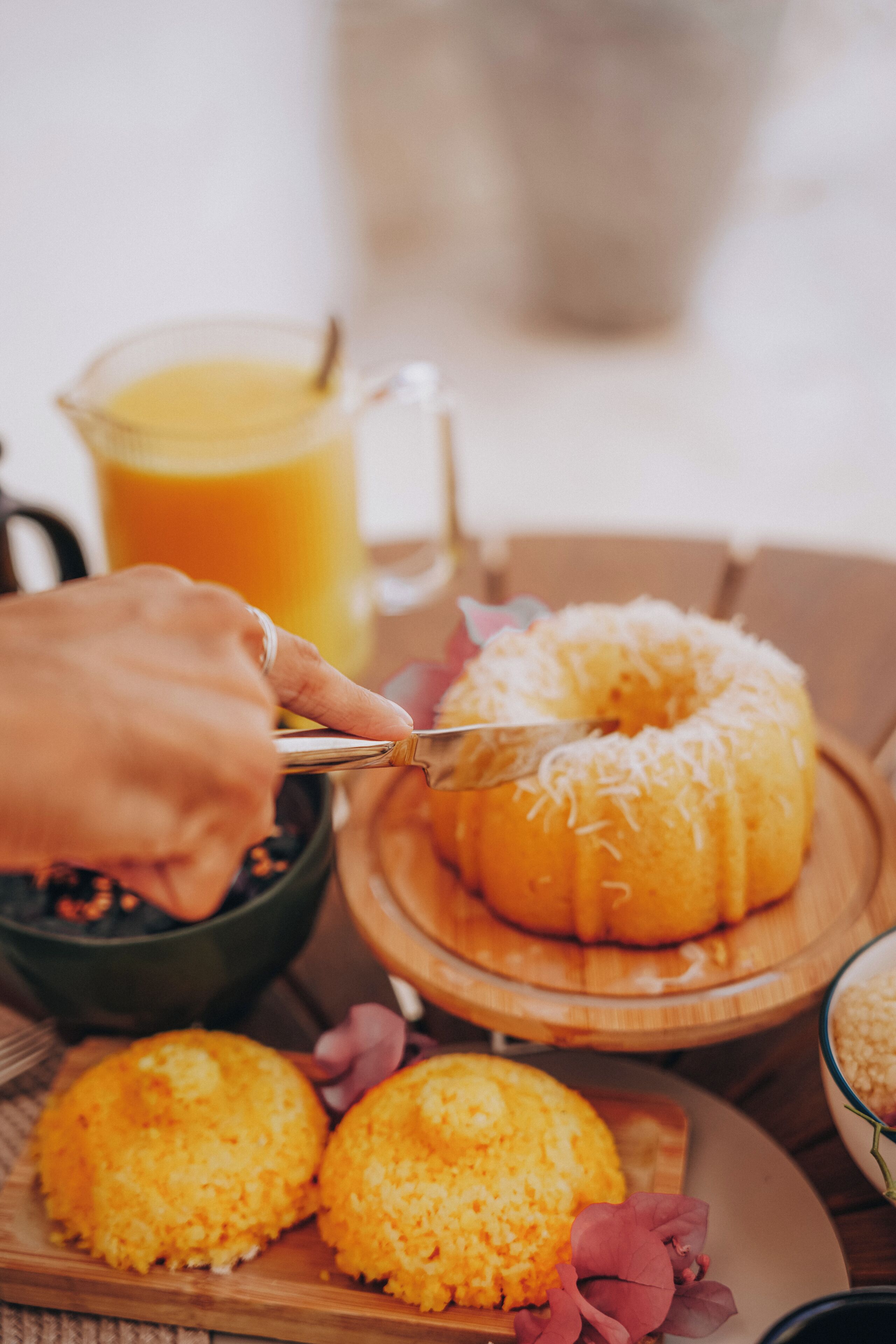 A hand cutting a donut, a glass of orange juice, and a plate with two muffins.