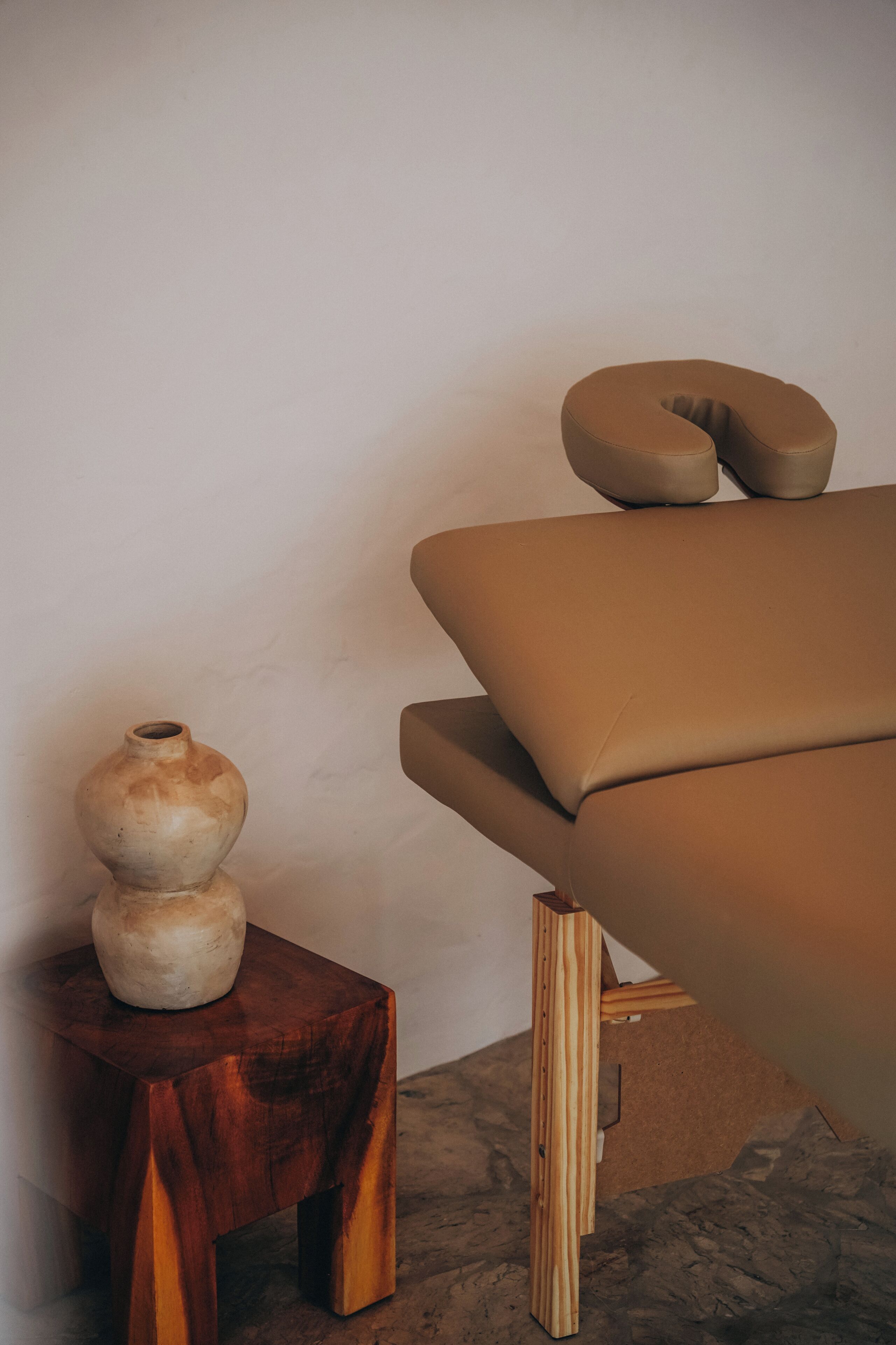 A room with a wooden stool, a vase, and a cushioned bench.