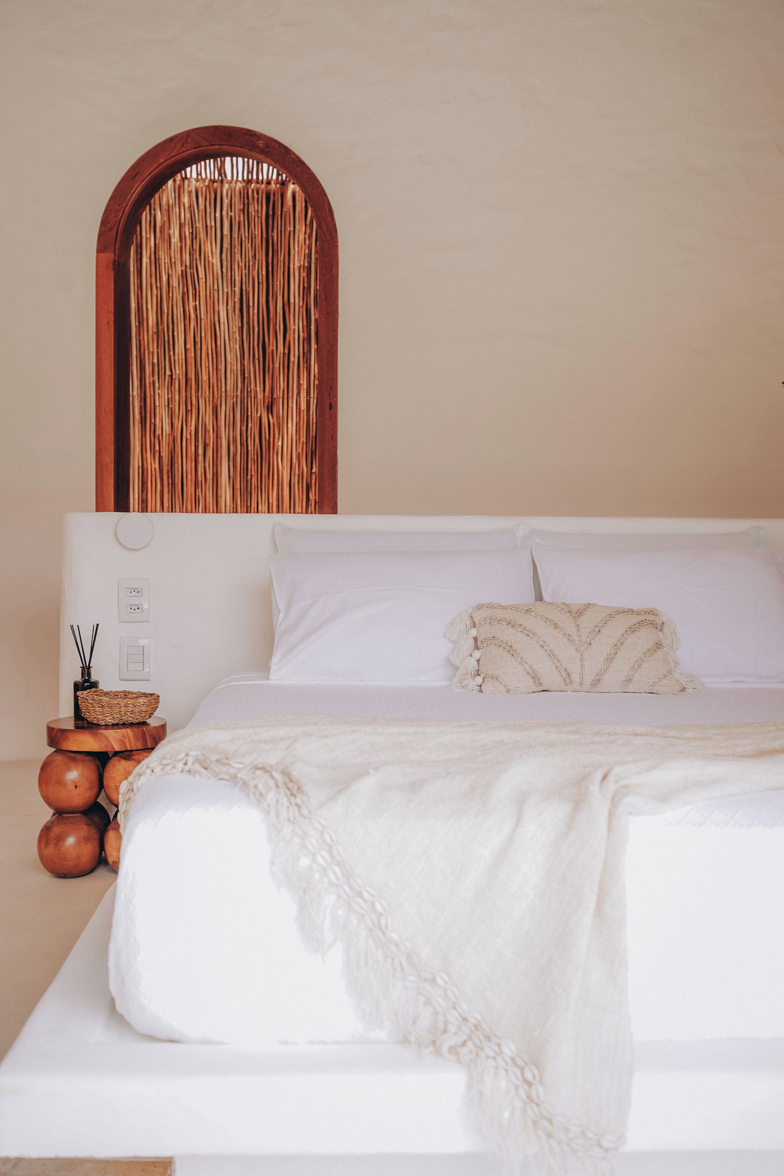 A bed with white linens, a wooden headboard, and a woven wall decoration.