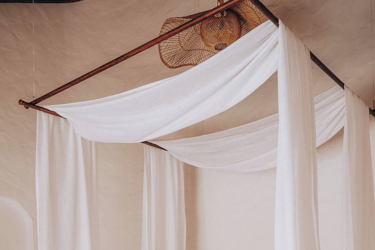 Una cama con dosel blanco y estructura de madera, con ropa de cama blanca.