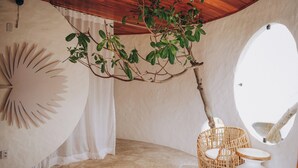 Ein Zimmer mit einem großen Spiegel, einem Korbstuhl, einem weißen Tisch, einem Ast und einem außergewöhnlichen Wanddesign.