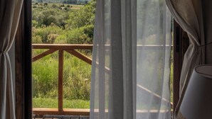 A room with a wooden balcony, a window with sheer curtains, and a lamp on the right side.