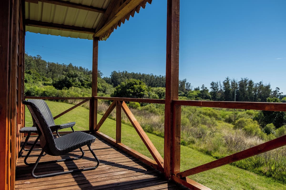 A wooden deck with a covered area, a chair, and a view of a green landscape.