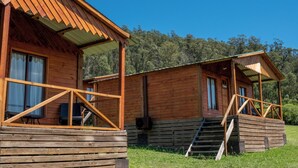 A wooden cabin with a porch, a staircase, and a view of the surrounding forest.