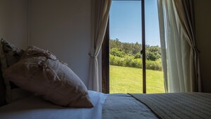 A bedroom with a bed, a pillow, and a view of a grassy area through a window. - Viña Edén (El Edén)