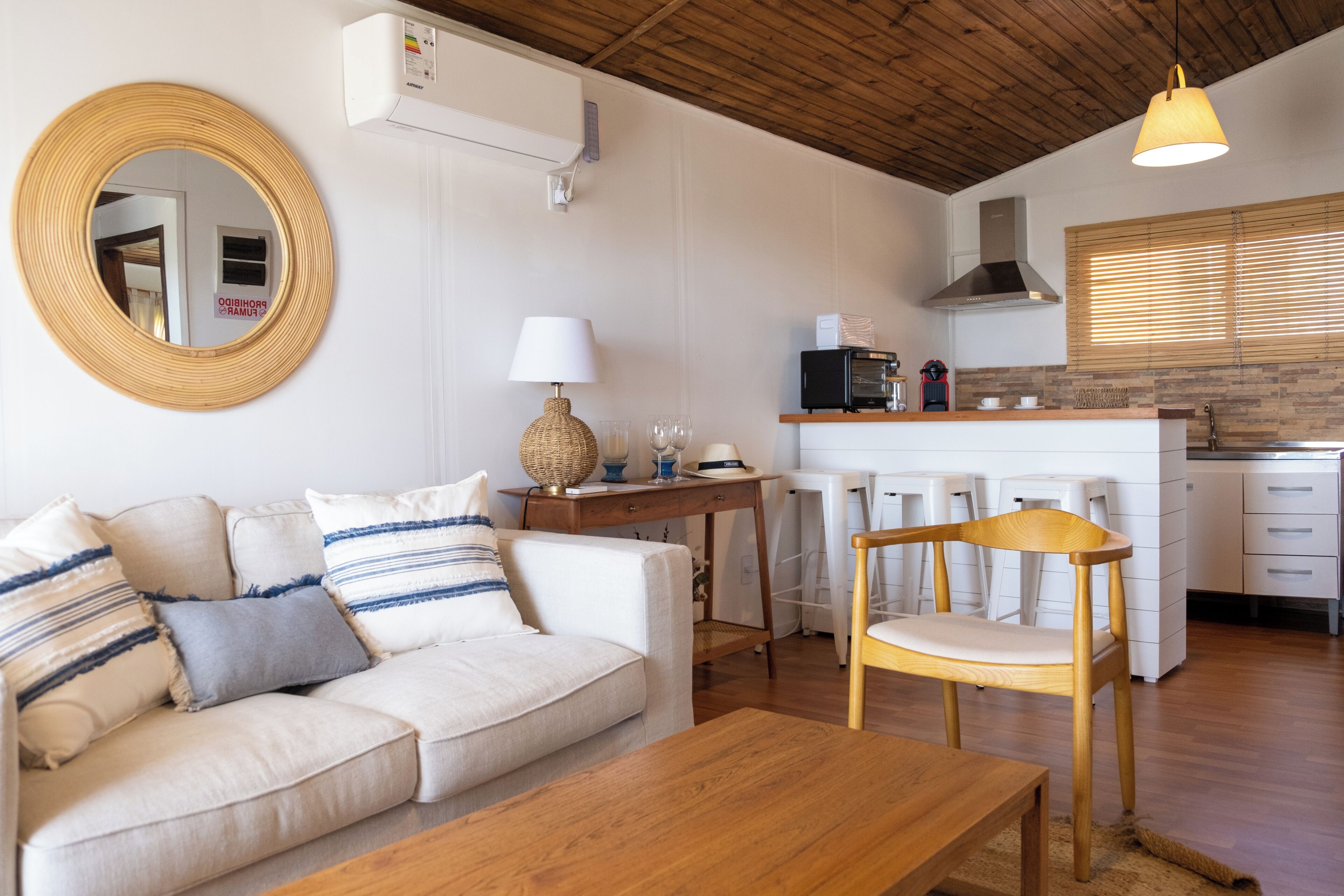 A living room with a sofa, a wooden table, a lamp, and a kitchen area with a stove and cabinets.
