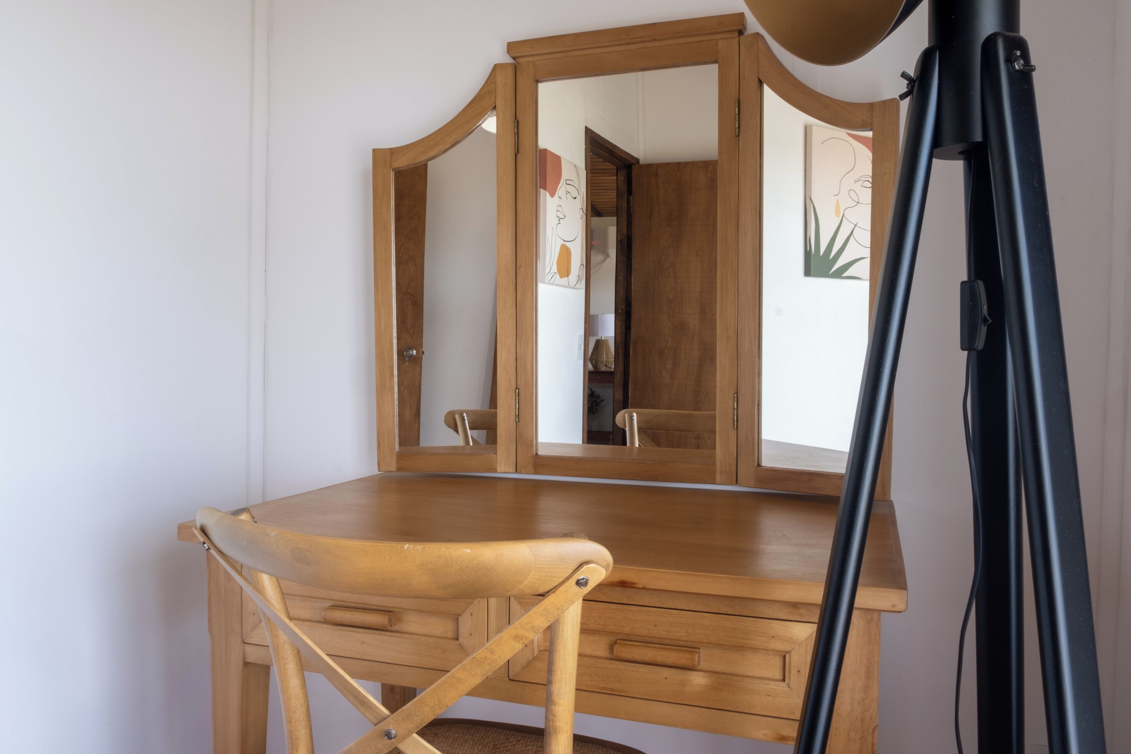 A wooden desk with a mirror and a tripod in a room with white walls.