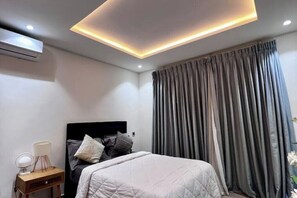A modern bedroom with a bed, bedside table, and a ceiling light fixture. - Luxury Studio apt with pool, close to airport (Accra)