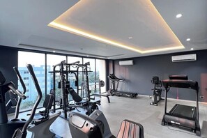 A modern gym with various exercise equipment, large windows, and a view of the city. - Luxury Studio apt with pool, close to airport (Accra)