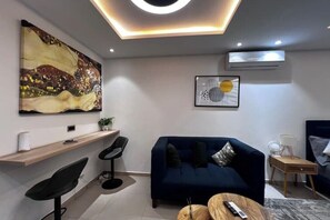 A modern living room with a dark blue sofa, a coffee table, and a large abstract painting on the wall. - Luxury Studio apt with pool, close to airport (Accra)