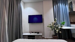 Une chambre d’hôtel moderne équipée d’un téléviseur à écran plat fixé au mur, d’une petite table avec des chaises et d’une plante en pot.