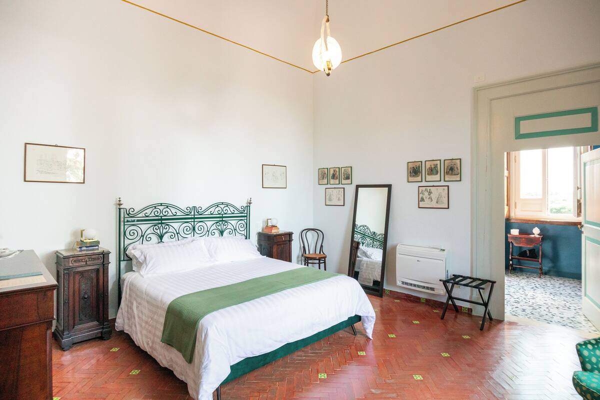 Ein Schlafzimmer mit Bett, Schminktisch, Sessel, Spiegel und Heizkörper.