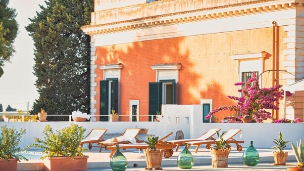 A rooftop terrace with lounge chairs, potted plants, and a building with a red facade and green shutters.