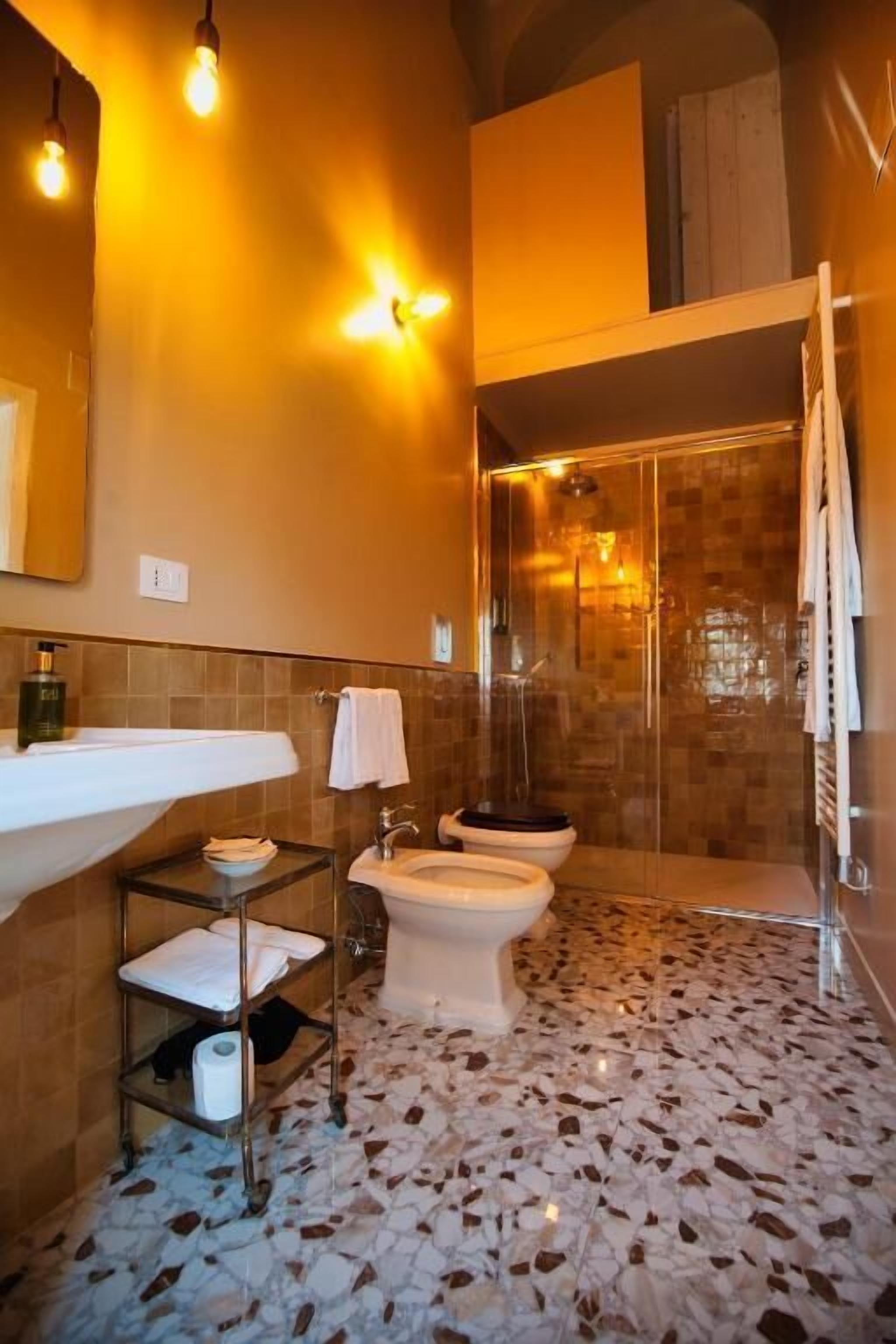 Une salle de bain avec un grand lavabo, deux toilettes, une douche et un sol carrelé.