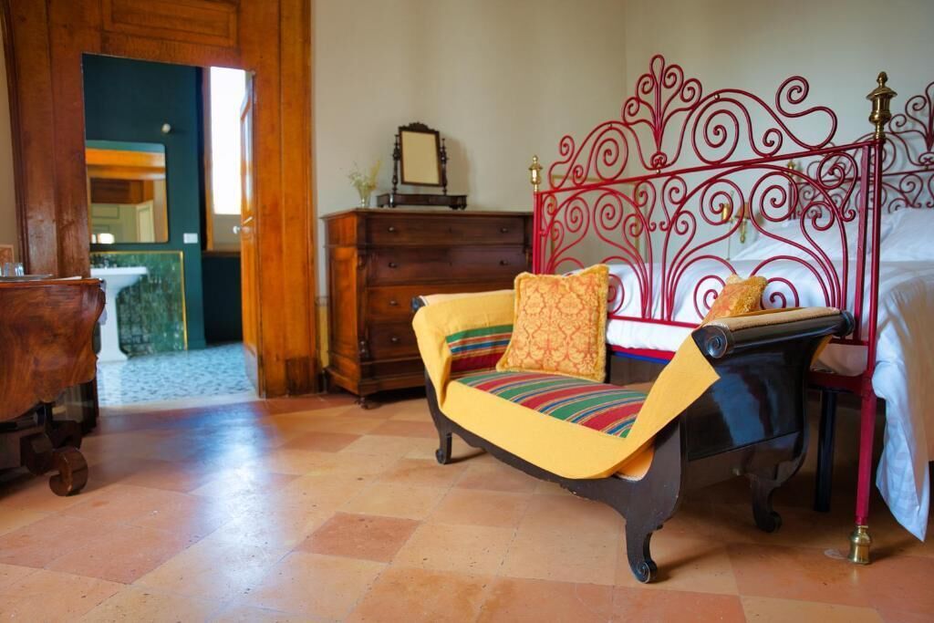 Una habitación con una cama, un aparador de madera, un cabecero metálico rojo y un sofá a rayas de colores.