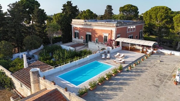 A rooftop swimming pool with lounge chairs, a covered seating area, and a building with a red facade. - Villa Ceci Dimora di Storie (Andria)