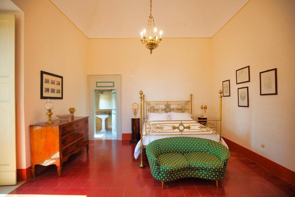 A bedroom with a bed, a dresser, a green armchair, and a chandelier.