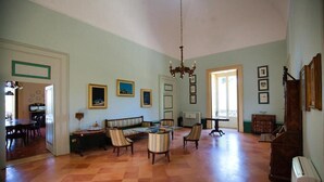 A spacious living room with a high ceiling, a chandelier, a dining area with a table and chairs, and a sofa.