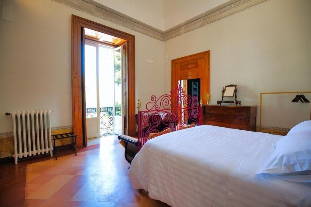A bedroom with a bed, a radiator, a wooden dresser, and a door leading to a balcony.