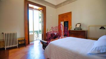 A bedroom with a bed, a radiator, a wooden dresser, and a door leading to a balcony.
