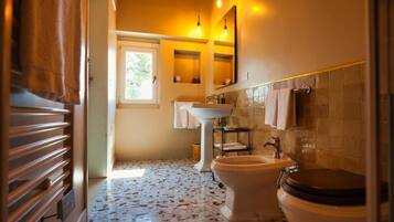Un bagno con lavabo a piedistallo, un water e una finestra che lascia entrare luce naturale.