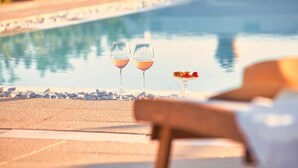 A poolside setting with two glasses of wine and a fruit plate.