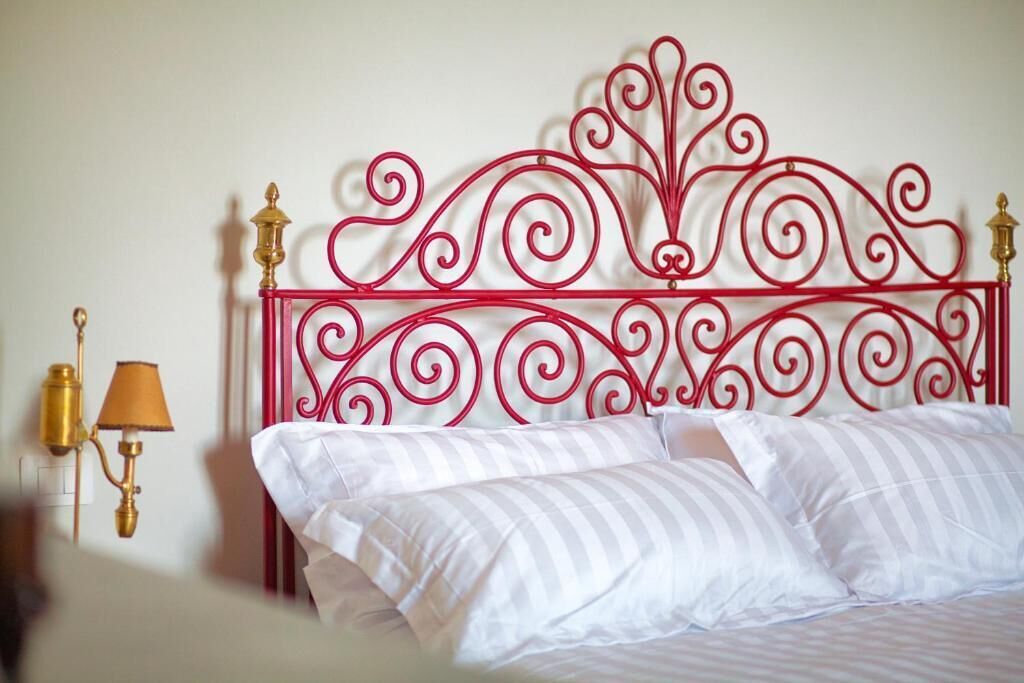 Een bed met witte strepen op het beddengoed en een rood metalen hoofdbord met gedetailleerde decoraties.
