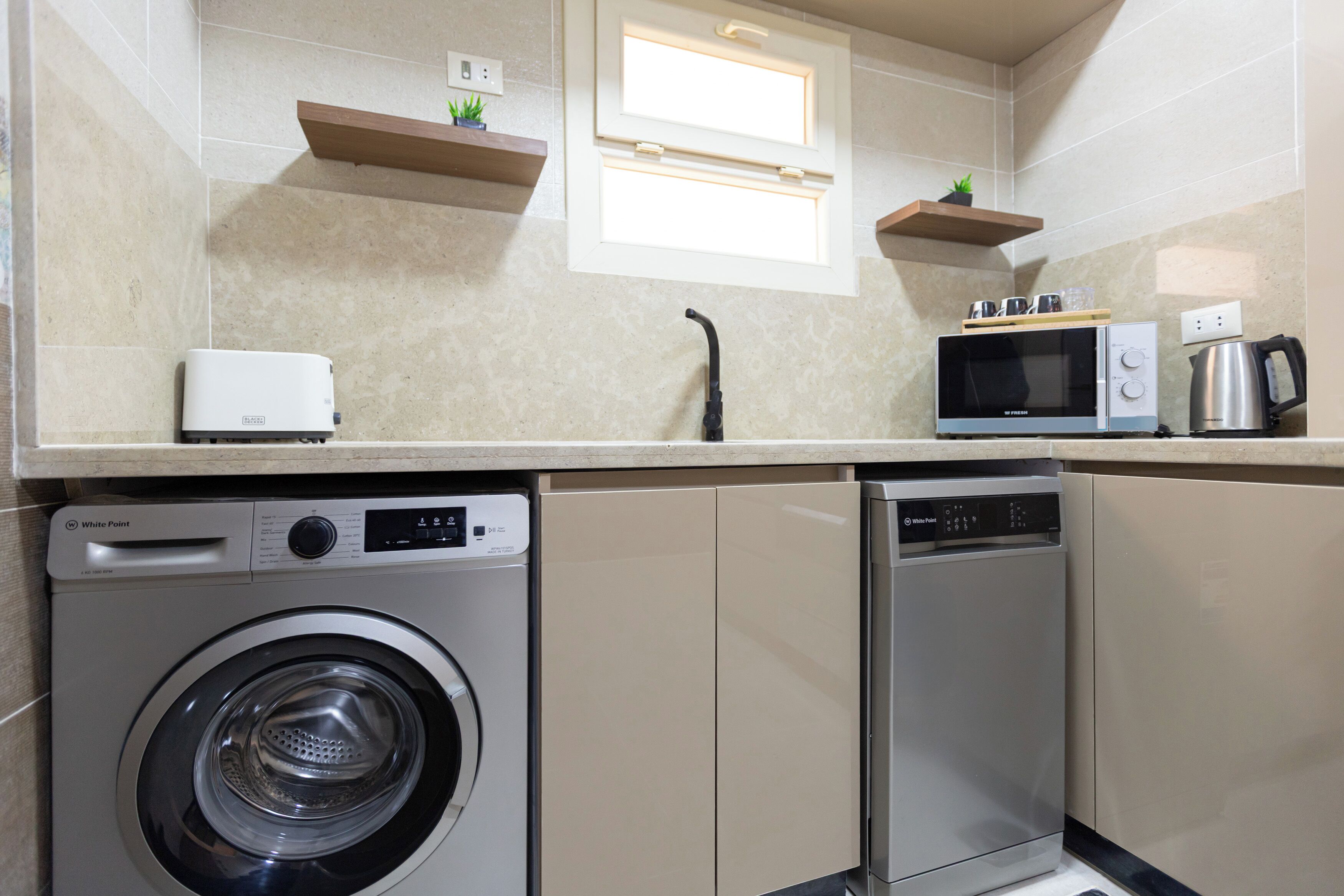 A compact kitchen with a washing machine, dishwasher, microwave, and a coffee maker.