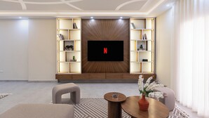 Een moderne woonkamer met een grote flatscreen televisie die aan een houten wand is bevestigd, omringd door ingebouwde planken met decoratieve objecten. Op de voorgrond staan twee banken en een salontafel.
