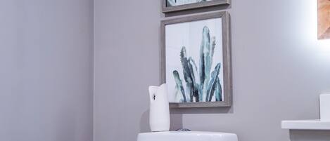 A modern bathroom with a white toilet, a trash bin, and two framed botanical prints on the wall.