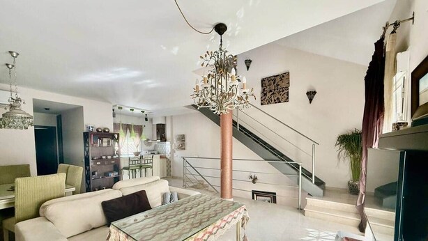 Un salon spacieux, doté d’un grand canapé, d’une table basse à motifs et d’un escalier menant à l’étage supérieur.