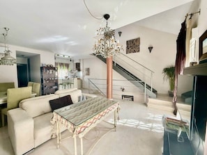 A spacious living room with a large sofa, a patterned coffee table, and a staircase leading to an upper floor. - Sonia Home Cordobesa (Córdoba)