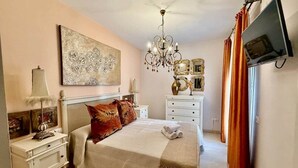 Une chambre à coucher avec un grand lit, un lustre, une télévision et un tableau au mur.