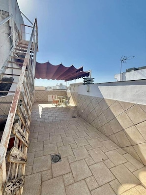 A rooftop terrace with a tiled floor, a metal staircase, a red canopy, and a few chairs. - Sonia Home Cordobesa (Córdoba)