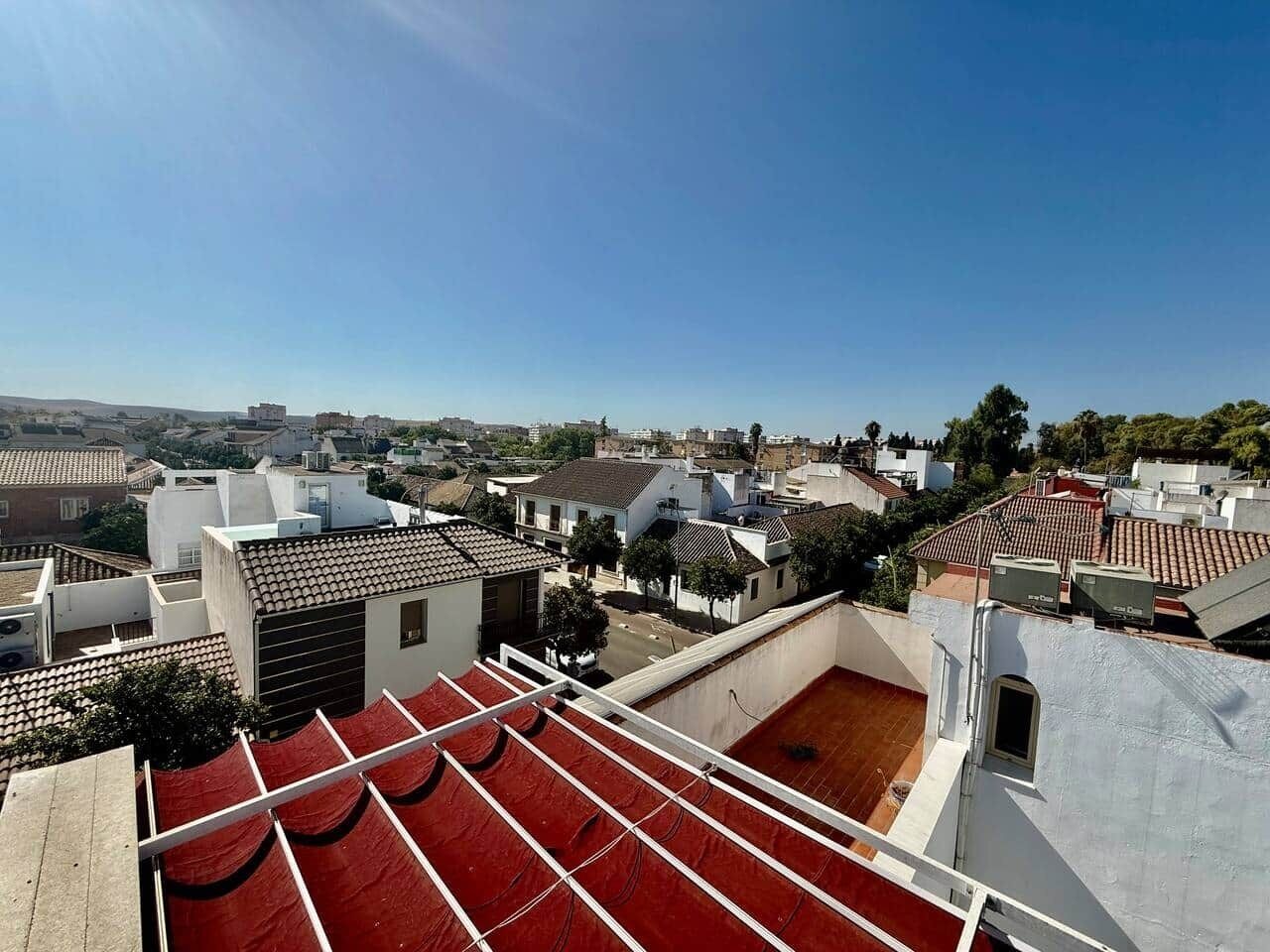 Una terraza en la azotea con toldos rojos, edificios blancos y un cielo azul despejado.