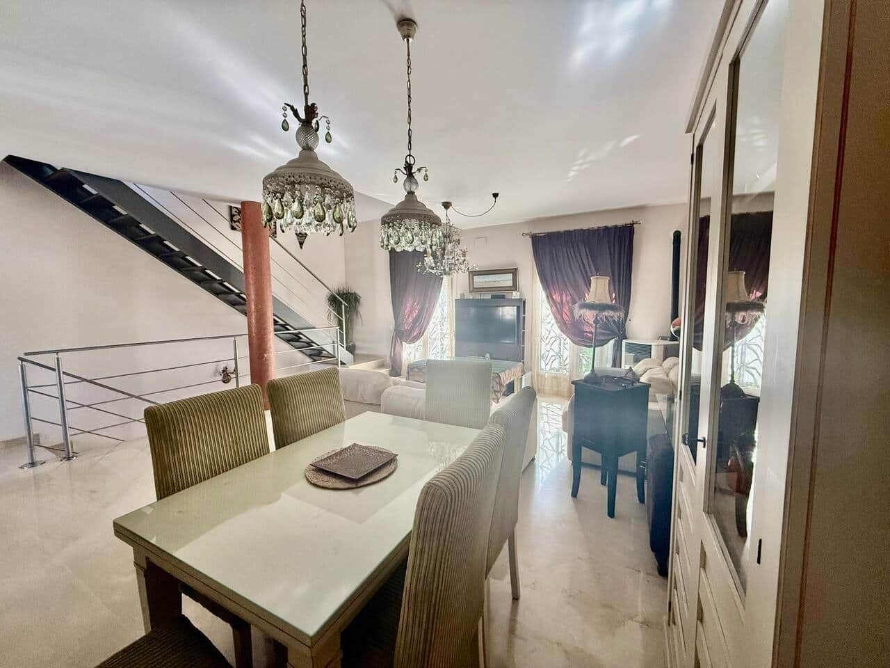 Amplia sala de estar con mesa de comedor, sillas y una escalera que sube a un piso superior.
