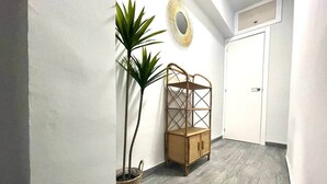 Um corredor com piso de madeira, uma mesinha de vime, um vaso com planta e uma porta branca.