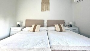 Uma cama de casal com duas mesas de cabeceira, um ar condicionado fixado na parede e um pendente de macramé.