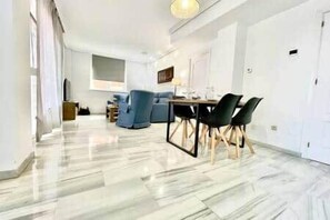 A modern living room with a dining area, marble flooring, and a large window. - Tendillas Penthouse: Córdoba Center (Córdoba)