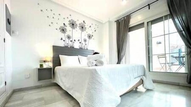 Ein modernes Hotelzimmer mit einem großen Bett, einem Nachttisch, einem Wandbild und Blick ins Freie durch ein großes Fenster.