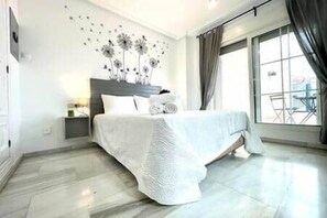 A modern hotel room with a large bed, a nightstand, a wall art piece, and a view of the outdoors through a large window. - Tendillas Penthouse: Córdoba Center (Córdoba)