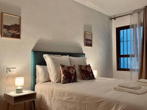 A neatly made bed with white linens and decorative pillows, a bedside lamp, and a window with sheer curtains. - San Luis Apartment (Córdoba)