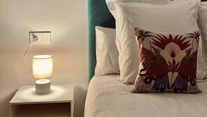 Un lit bien fait, avec du linge de lit blanc et une tête de lit couleur turquoise, une lampe de chevet et un tableau encadré au mur.