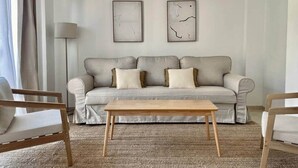 Un salon avec un canapé gris, deux œuvres d’art abstraites encadrées, une table basse en bois et deux chaises en bois.