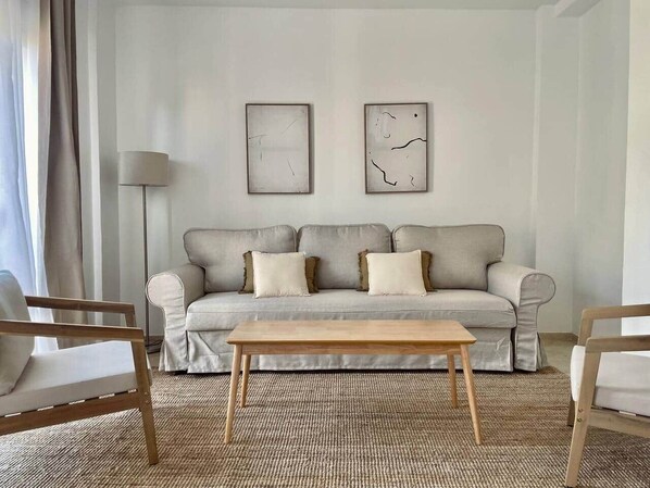 A living room with a grey sofa, two framed abstract artworks, a wooden coffee table, and two wooden chairs. - San Luis Apartment (Córdoba)