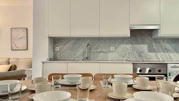 Cozinha moderna com armários brancos, painel de mármore e mesa de jantar posta para seis, com pratos, tigelas e copos brancos.