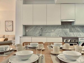A modern kitchen with white cabinets, a marble backsplash, and a dining table set for six with white plates, bowls, and glasses. - San Luis Apartment (Córdoba)