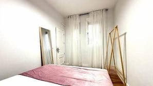 Un dormitorio con una cama, un ventanal con cortinas, una puerta y suelo de madera.