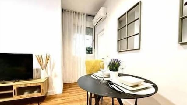 Una sala de estar moderna con un televisor de pantalla plana, una mesa de comedor redonda y un sillón amarillo.