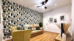 Una sala de estar moderna con un papel tapiz estampado, suelo de madera, un sofá amarillo y un ventilador de techo.